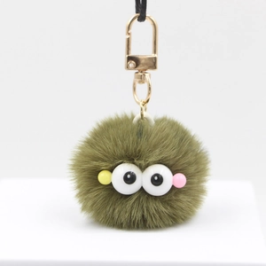 Close-up of fluffy green pompom charm with cartoon eyes and golden metal clasp