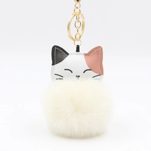 Close-up of cute lucky cat keychain with soft white pompom and golden metal ring
