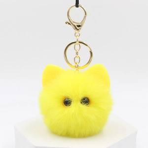 Close-up of fluffy yellow kitten plush keychain with golden metal clasp on white stand