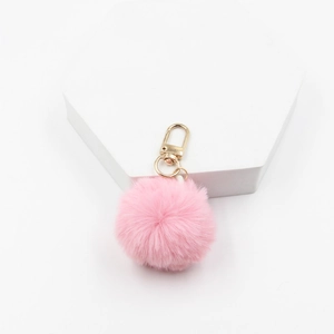 Detailed view of soft pink faux fur pompom keychain with golden metal spring clasp on stand