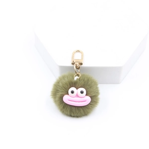 Detail shot of olive green plush pompom keychain with quirky big eyes on white stand