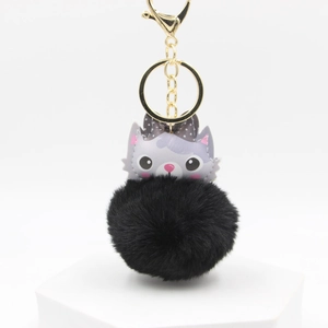 Close-up of cute grey cat pendant with soft black faux fur pom pom and golden keychain