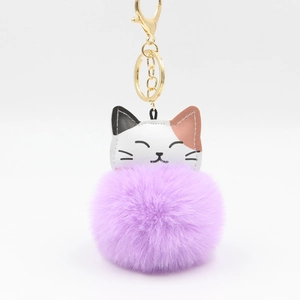 Close-up of a purple fluffy pompom lucky cat keychain with white and brown faux leather