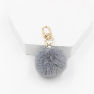 Close-up of soft grey faux fur pompom keychain with light gold metal clasp details