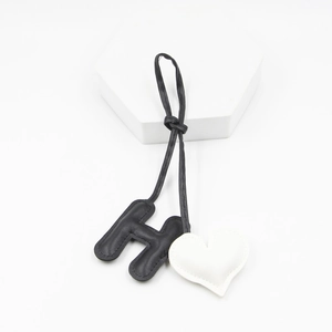 Close-up of black leather letter H and white heart charm pendant for handbags