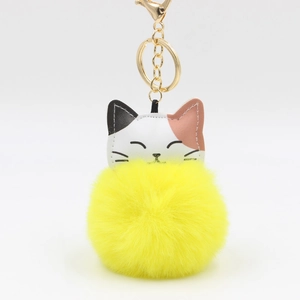 Detail of yellow plush pom-pom keychain with tricolor leather cat head and gold hardware