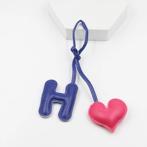 Detailed view of handmade blue leather H-letter and pink heart bag charm with fine stitching