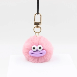 Macro detail of a soft pink furry pom-pom keychain with cartoon face and gold hardware