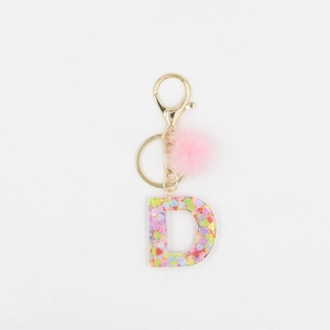 Détail du porte-clés lettre D en résine pailletée avec pompon rose et clip doré