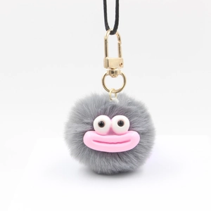 Close-up of grey plush ball keychain with a funny cartoon face and golden metal clasp