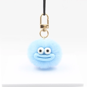 Cute light blue furry ball keychain with cartoon face and gold metal clasp on white stand