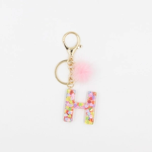 Détail du porte-clés lettre H avec paillettes en cœur et pompon en peluche rose