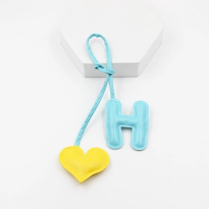 Detail of blue leather letter H and yellow heart charm with fine stitching on white background