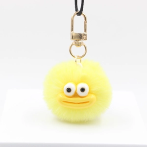 Detail of a bright yellow furry monster keychain with a golden clasp and funny cartoon face