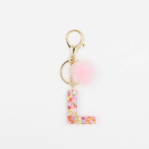 Détail de boule de poils rose et porte-clés lettre L en résine avec paillettes cœur