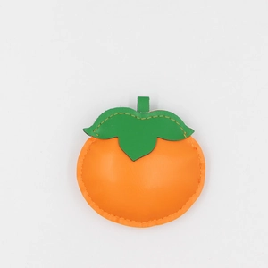 Macro view of bright orange leather persimmon charm with green leaves and yellow stitching