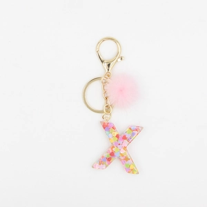 Détail macro du porte-clés lettre X avec paillettes colorées et pompon en fourrure rose