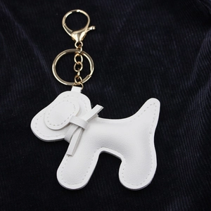 Détail d'un porte-clés chien en cuir blanc avec attaches dorées et surpiqûres