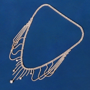 Close-up of golden fringe necklace with cascading rhinestones on navy textured background