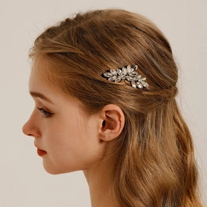Détail d'un peigne à cheveux de mariée avec feuilles en cristal sur des cheveux bruns ondulés
