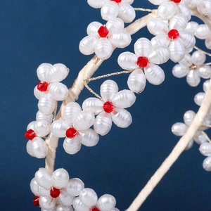 Detail of white handmade pearl flower headband featuring faceted red crystal center beads