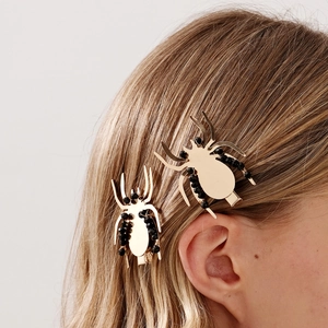 Détail de la pince à cheveux araignée dorée avec perles noires dans des cheveux blonds