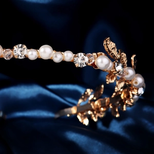 Detailed close-up of golden headband with pearls and crystals on blue silk background