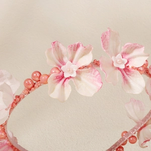 Nahaufnahme von rosa-weißen Stoffblumen mit Perlenquasten-Details auf einem Kinderhaarreif