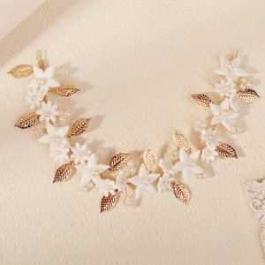 Handmade bridal hair comb with white clay flowers, pearls and golden leaves on a soft background