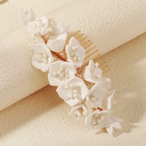 Detailed view of white floral hair comb with pearls and gold metal wiring for brides