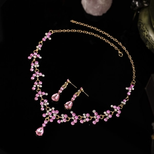 Détail de la parure collier et boucles d'oreilles dorée avec strass roses sur fond noir