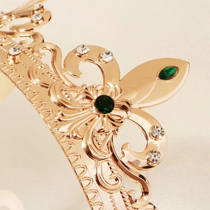 Macro shot of gold baroque crown detailing with green gemstones and intricate scrollwork