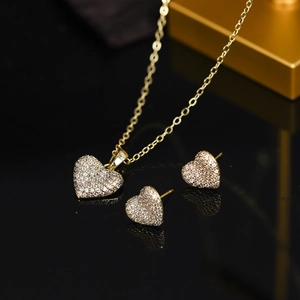 Detailed view of heart necklace and earrings set with shimmering zircon in golden finish
