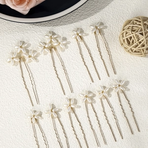 Macro view of 11 golden U-shaped hairpins with white pearl flower decor on white background
