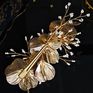 Detail of handmade gold metal petal hair clip with white pearl beads on black surface