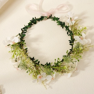 Detailed view of green leaf floral wreath headband with white fabric flowers and pink ribbon