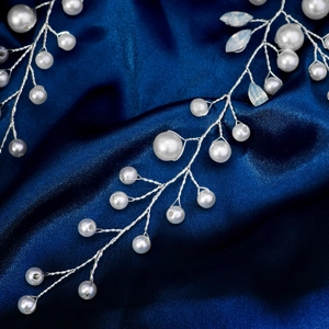 Détail d'une pince à cheveux en perles avec fil argenté sur un tissu en soie bleue