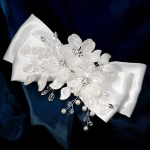 Détail de la barrette à nœud en satin blanc avec fleurs acryliques et perles élégantes