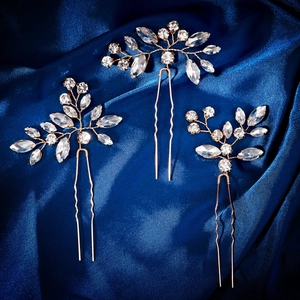 Detail of three gold leaf-shaped U-shaped hair pins with shimmering rhinestones on blue silk