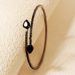Detail view of black rhinestone open cuff bracelet with teardrop stones on textured surface