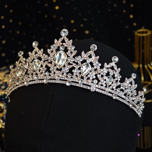 Dettaglio della corona dorata con cristallo a goccia e strass brillanti su supporto nero