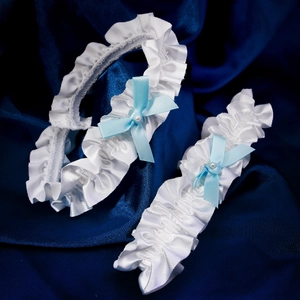 Close-up of white satin bridal garters with blue bows and pearls on blue background