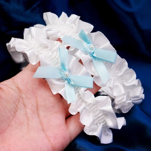 Close-up of white satin bridal garter set with blue bows and pearl details