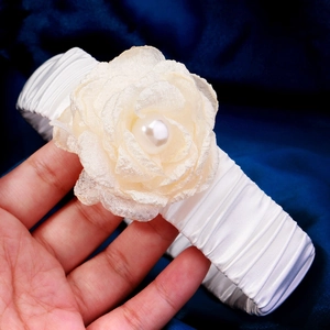 Close-up of white satin headband with a beige silk flower and a center pearl detail