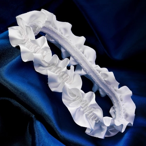 Detail of white satin ruffled garter with elastic band on dark blue silk background