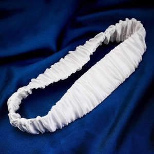 Detail of white ruffled satin bridal garter on elegant dark blue silk background