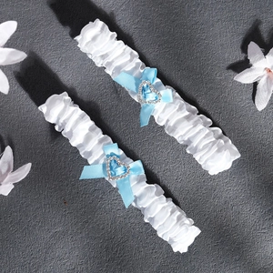 Close-up of white lace bridal garters with blue satin bows and heart crystal accents