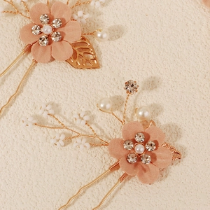 Close-up of pink fabric flower hair pins with pearls, gold leaves and rhinestones
