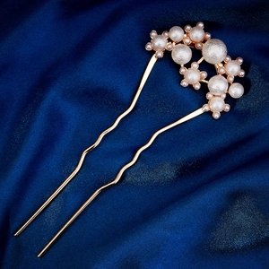 Macro shot of gold U-shaped hairpin with clustered pearls against blue silk fabric