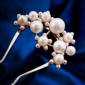 Detailed macro view of gold-tone U-shaped hair pin with elegant white pearls on navy velvet
